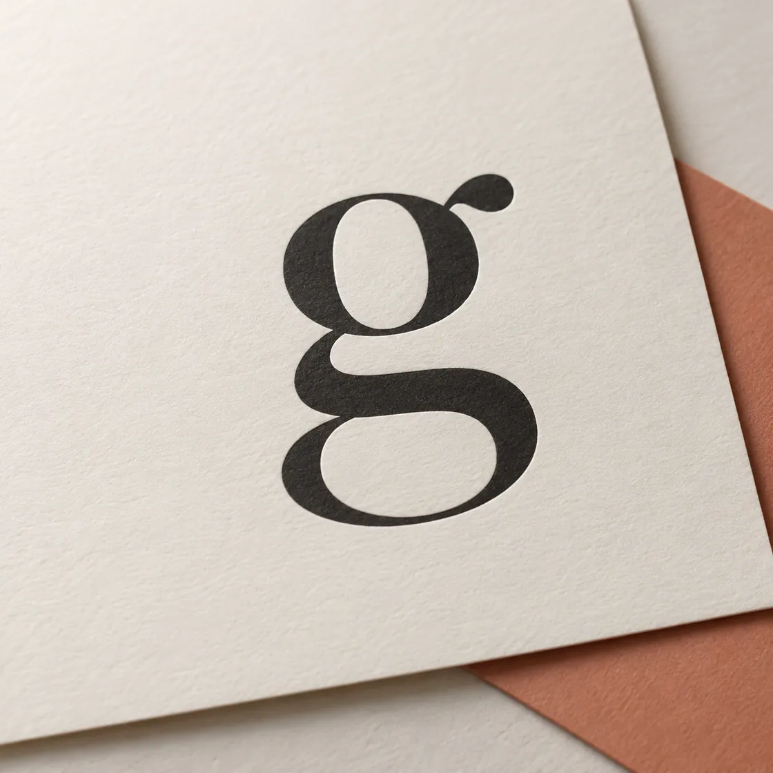 A lowercase serif g printed in black on ivory paper, a terracotta sheet beneath
